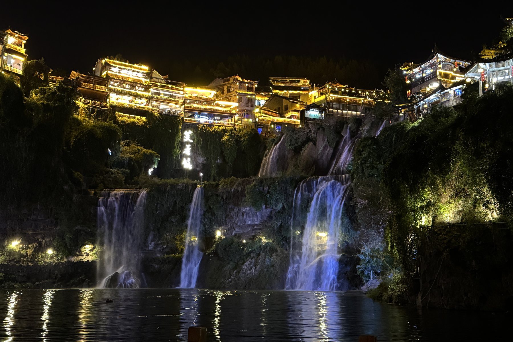 Furong Town at night, the waterfall that runs through the middle of the old town dropping into the Youshui river below the lit stilt houses