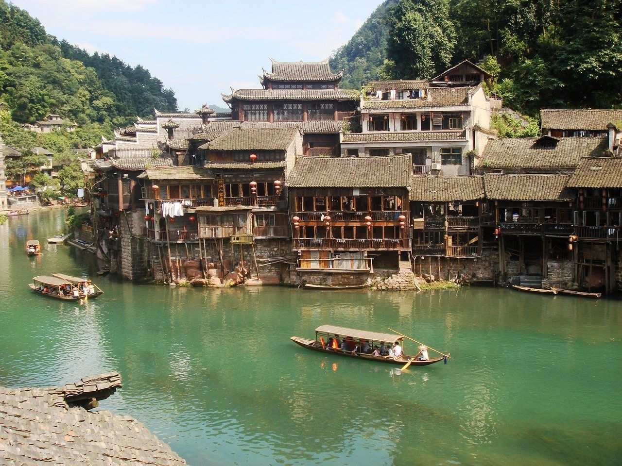 Timber stilt houses above the Tuo river in Fenghuang — the stretch of old town that costs nothing to walk through