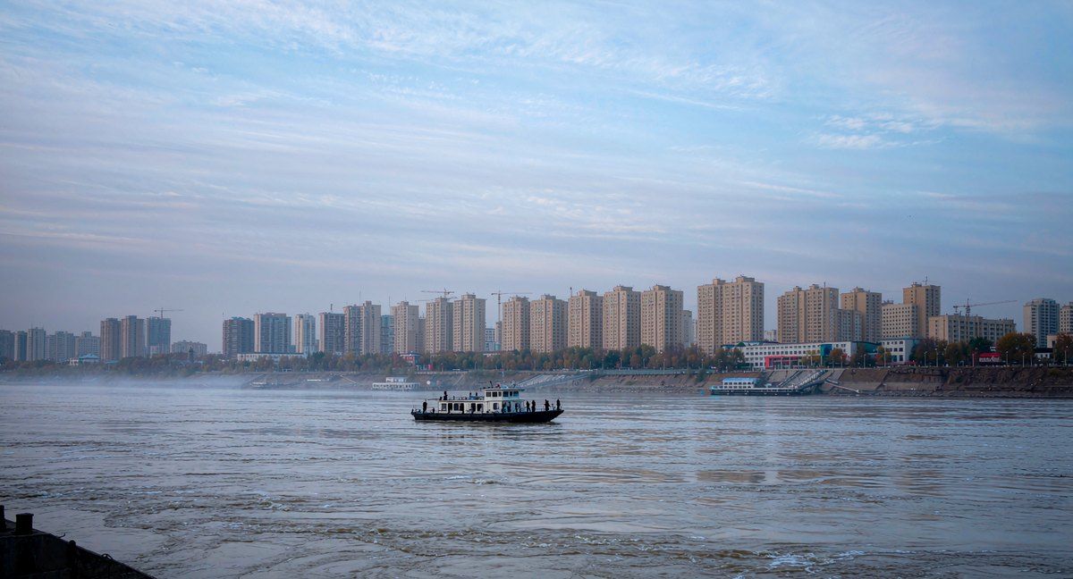 A passenger ferry crossing a wide border river toward a city skyline of apartment blocks on the far bank — AI-generated illustration, not a photograph of the actual crossing
