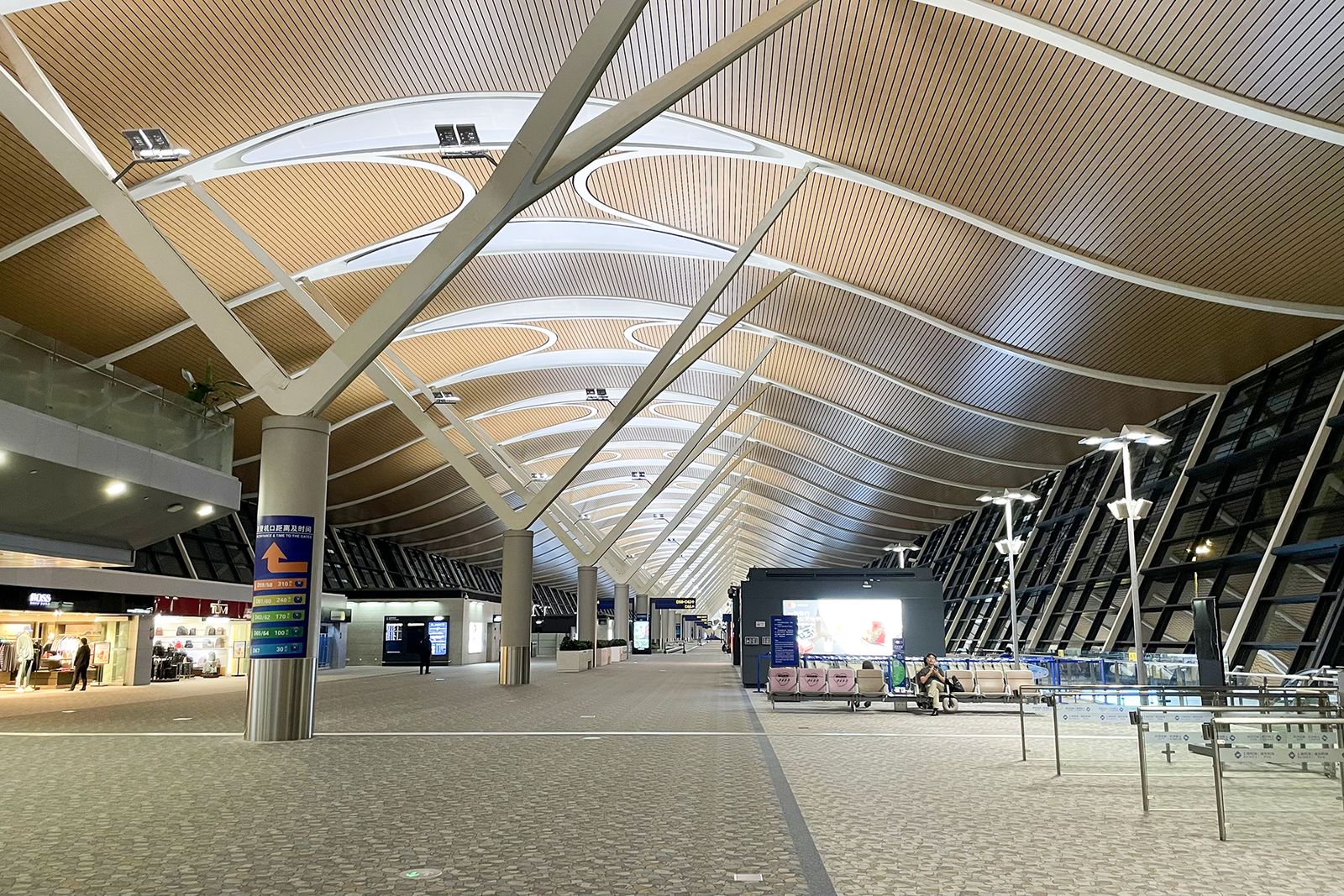 An airside corridor inside Terminal 2 at Pudong, with rows of seats and a sign pointing to exits and baggage reclaim