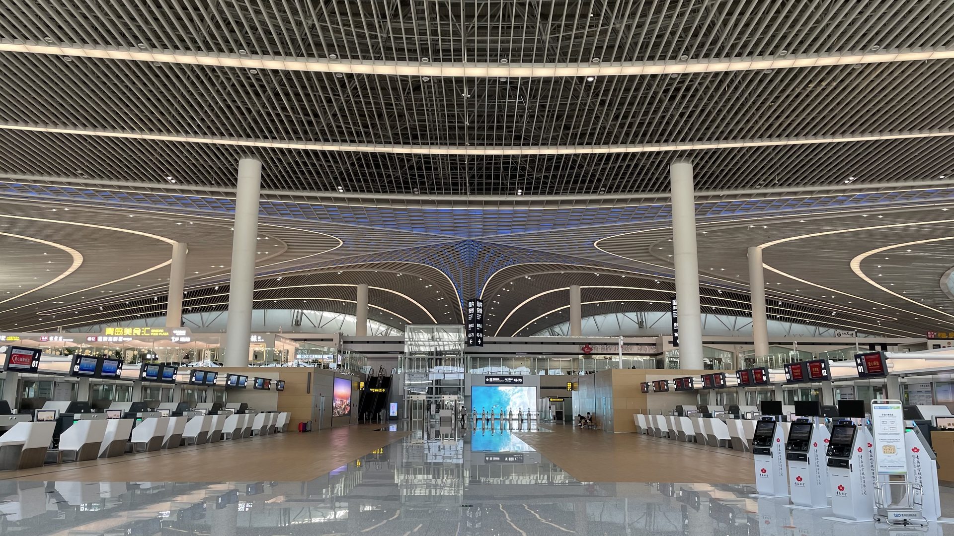 Interior of Qingdao Jiaodong Airport Terminal 1 with check-in counters and sweeping curved ceiling — Photo: Ginbayashi / CC BY-SA 4.0 via Wikimedia Commons