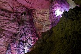 Interior of Huanglong Cave near Zhangjiajie: a tall flowstone column and hanging stalactites lit in pink and violet — Photo: Dimain69 / CC BY-SA 3.0 via Wikimedia Commons
