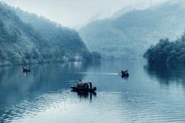 Misty morning on the Xiaodongjiang section of Dongjiang Lake, Hunan, with small fishing boats drifting through river fog — Photo: 伊口 / CC BY 2.5 via Wikimedia Commons