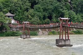 The Anlan suspension bridge over the Min River at Dujiangyan, with red timber pylons and white water below — Photo: xiquinhosilva / CC BY 2.0 via Wikimedia Commons