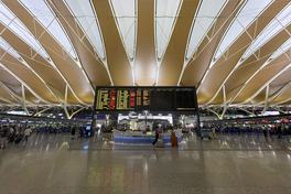 The departures concourse at Terminal 2 of Shanghai Pudong International Airport, its wave-patterned ceiling arched over the flight information board and service desk — Photo: Windmemories / CC BY-SA 4.0 via Wikimedia Commons