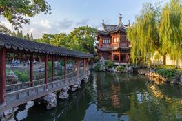 A covered walkway and waterside pavilion inside Yu Garden, Shanghai, with rockeries and willows reflected in the pond — Photo: Stefan Fussan / CC BY-SA 3.0 via Wikimedia Commons