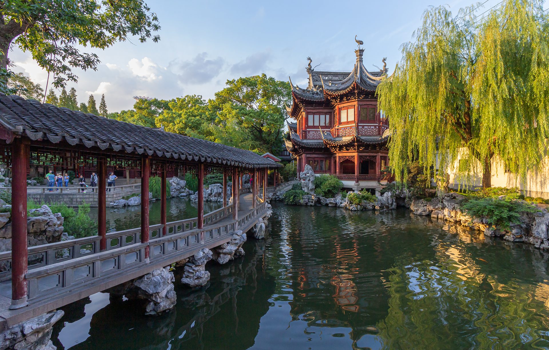 A covered walkway and waterside pavilion inside Yu Garden, Shanghai, with rockeries and willows reflected in the pond — Photo: Stefan Fussan / CC BY-SA 3.0 via Wikimedia Commons